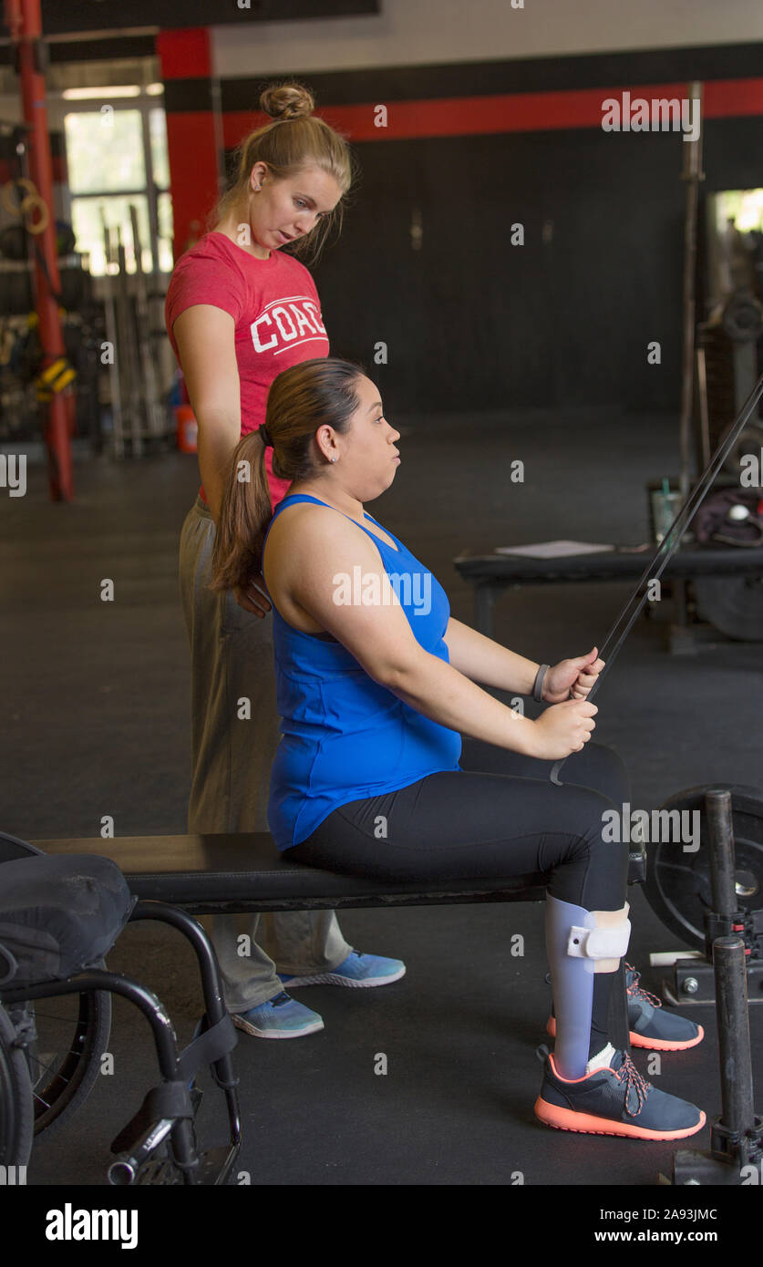 Mujer con lesión de la médula espinal haciendo ejercicio en un gimnasio con un entrenador Foto de stock