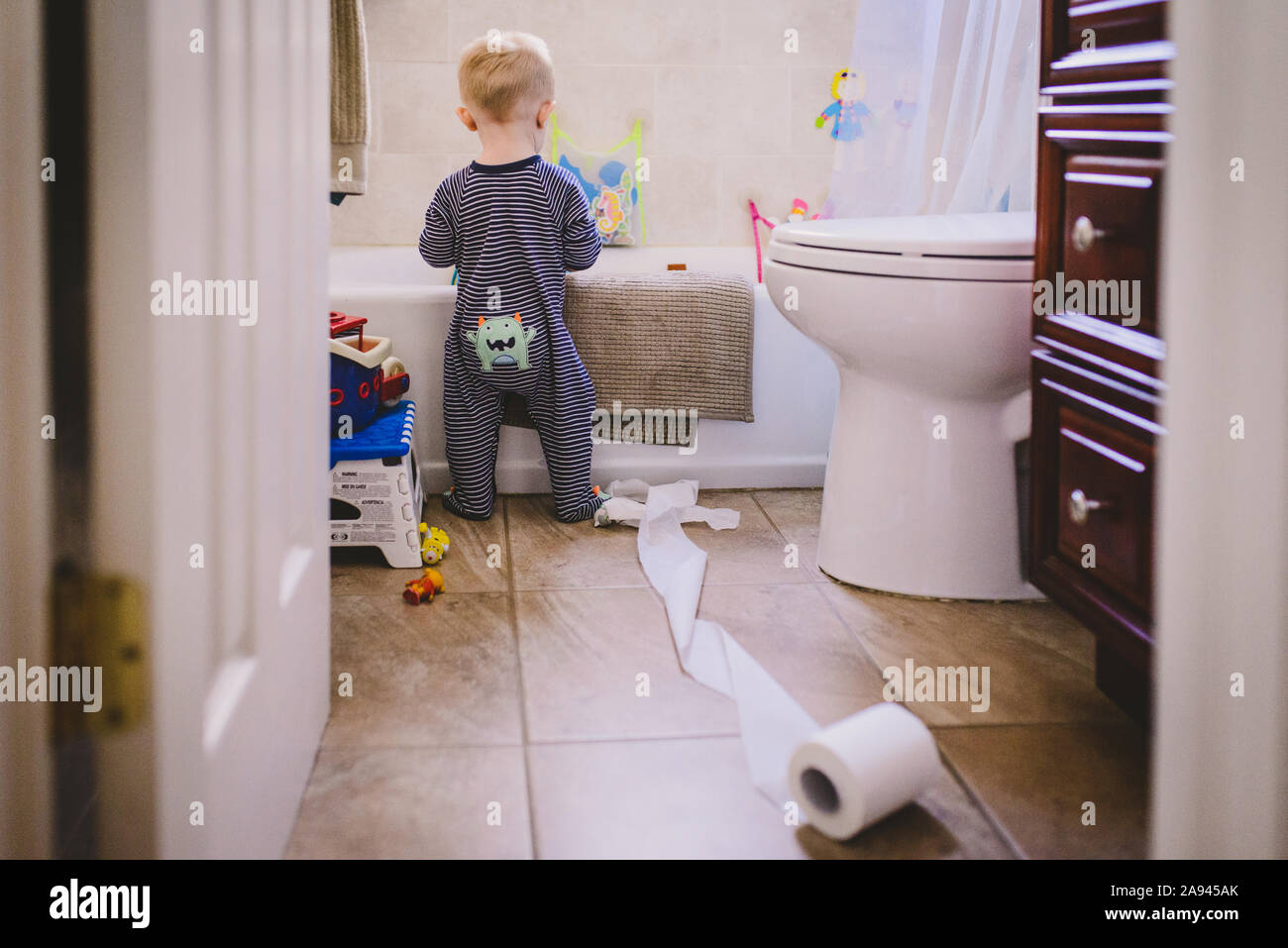 Un niño se encuentra en un cuarto de baño con un rollo de papel higiénico develada. Foto de stock