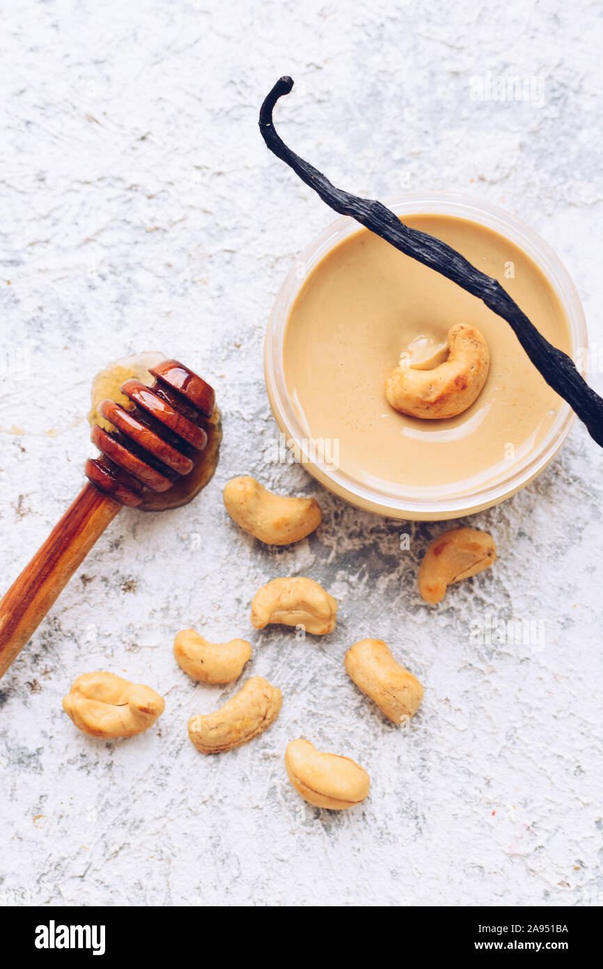 Nuez de mantequilla en el vidrio. Materias orgánicas caseras anacardos pegar sobre fondo gris con la miel y la vainilla. Concepto de alimentos naturales saludables. Vista desde arriba. Foto de stock