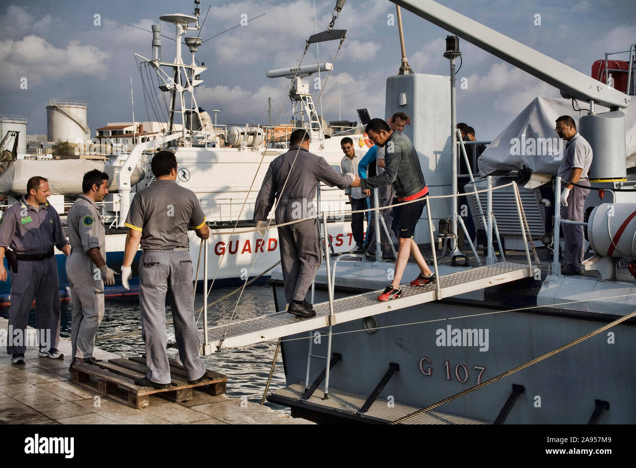 Oficiales de la Guardia di Finanza, ayudando a los inmigrantes ilegales para sacar el barco después de una operación de rescate Foto de stock