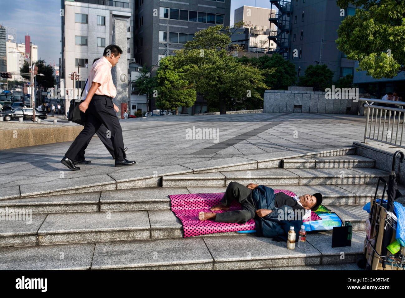El hombre camina más allá de un Homeless durmiendo en la acera Harumi dori, Tokio, Japón. Foto de stock