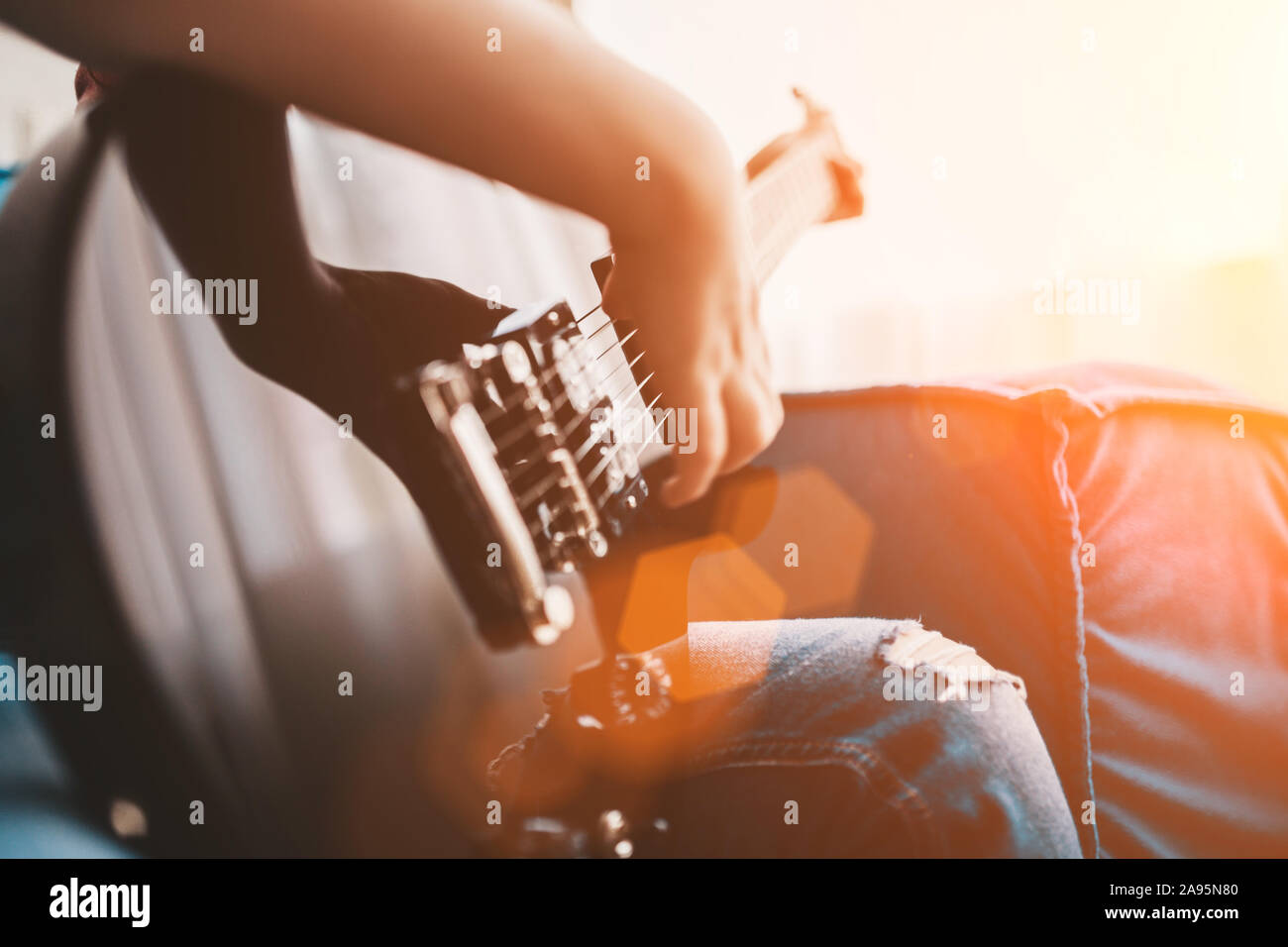 Primer plano de un niño tocando una guitarra eléctrica negra - la mano golpea las cuerdas Foto de stock