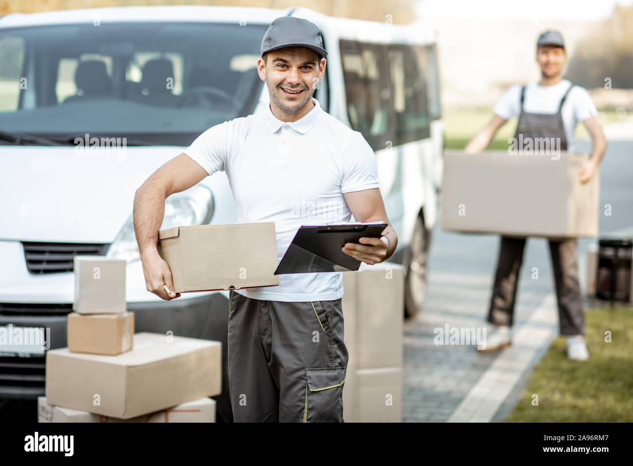 Retrato del hombre en la entrega uniforme con documentos permanente cerca  del vehículo camioneta de carga, colega descarga paquetes sobre el fondo  Fotografía de stock - Alamy
