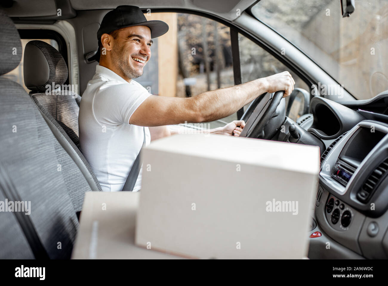 Hombre de entrega de conducción de vehículos de carga con bultos en el asiento del pasajero, vista interior del vehículo en los cuadros con espacio en blanco Foto de stock