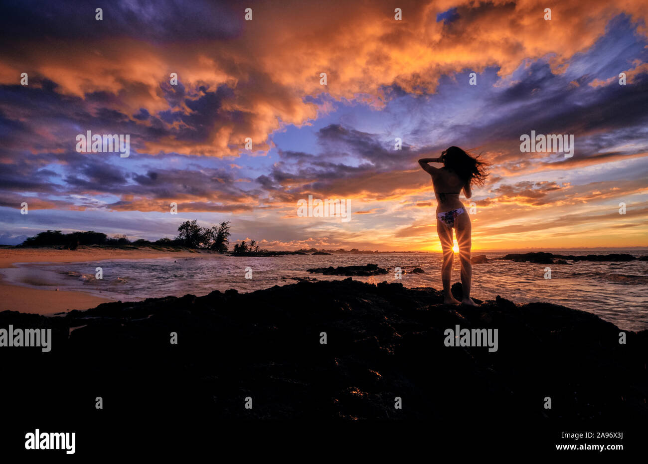 Una joven mujer se detiene para celebrar la puesta de sol sobre la playa Makalawena Hawaii Foto de stock