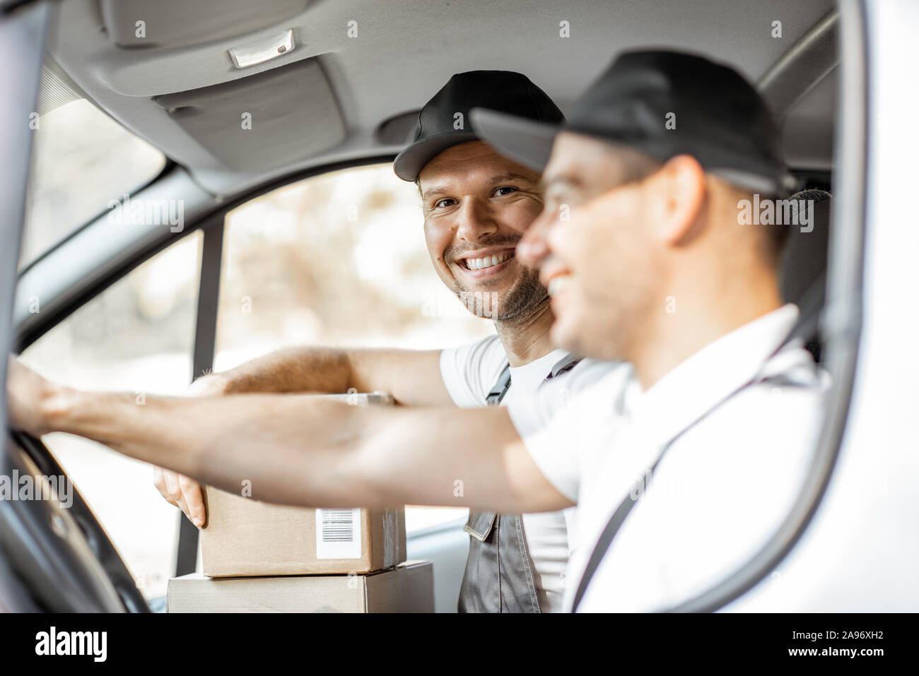 Dos empleados de la compañía de entrega alegre en uniforme divertirse mientras se conduce un vehículo de carga, la entrega de bienes a los clientes Foto de stock