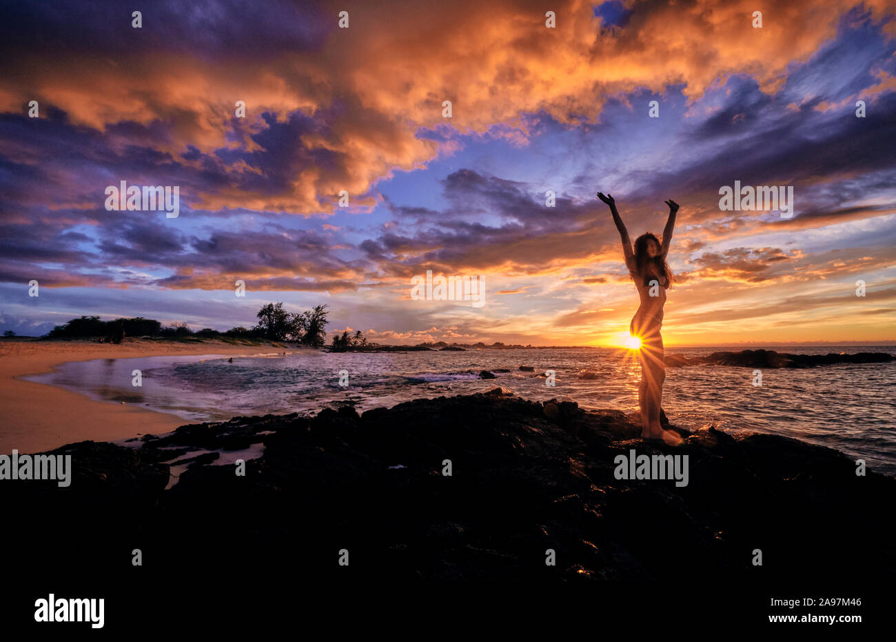 Una joven mujer se detiene para celebrar la puesta de sol sobre la playa Makalawena Hawaii Foto de stock