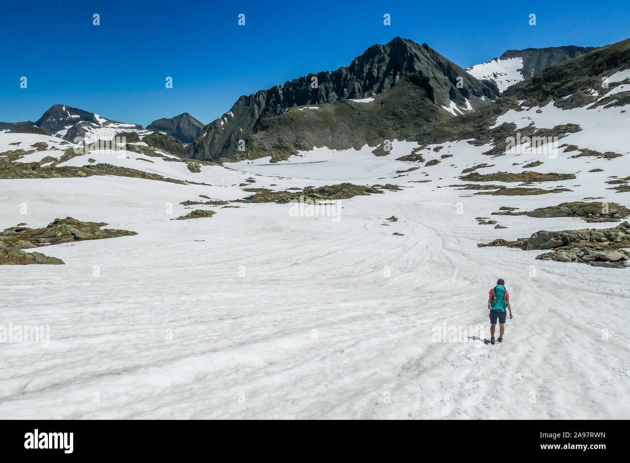 Una mujer joven con una mochila grande caminatas a través de una meseta de  nieve en las altas montañas. Chica es usar pantalones cortos.En la parte de  atrás hay un fuerte pico
