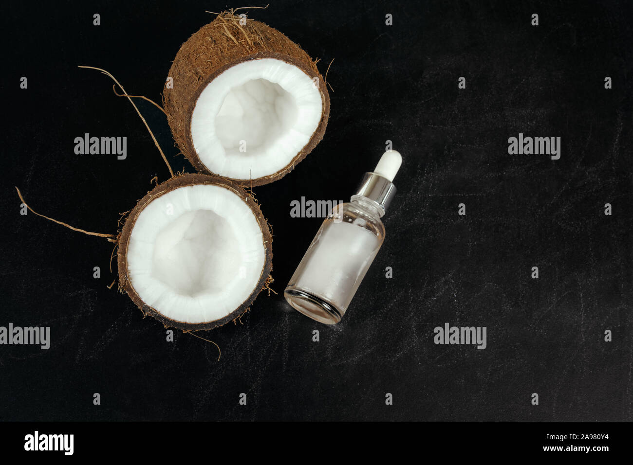 Mitades de coco y la botella de aceite de coco en pizarra negra con espacio libre para texto Foto de stock