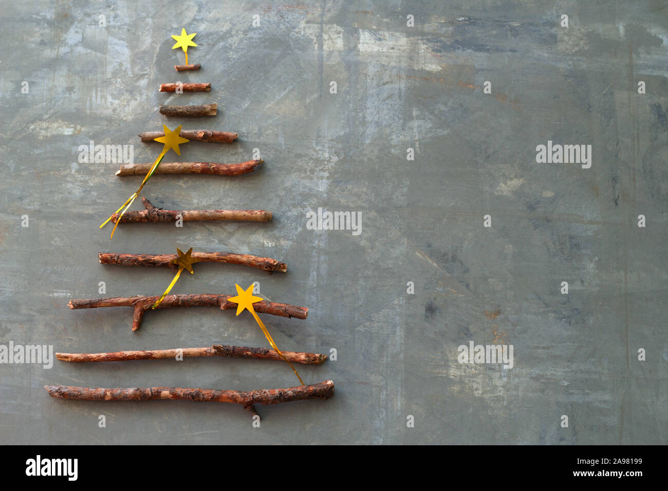 Vista superior plana silueta laicos de un árbol de Navidad hecho de ramitas de madera decorado con estrellas doradas lentejuelas sobre un fondo de cemento gris con espacio para t Foto de stock