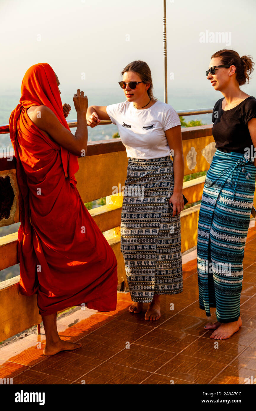 Dos mujeres turistas hablando a un grupo de monjes budistas, Su Taung Pyae Pagoda, Mandalay Hill, Mandalay, Myanmar. Foto de stock