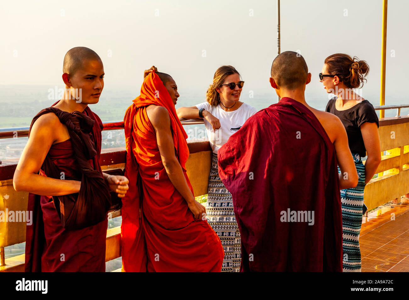 Dos mujeres turistas hablando a un grupo de monjes budistas, Su Taung Pyae Pagoda, Mandalay Hill, Mandalay, Myanmar. Foto de stock