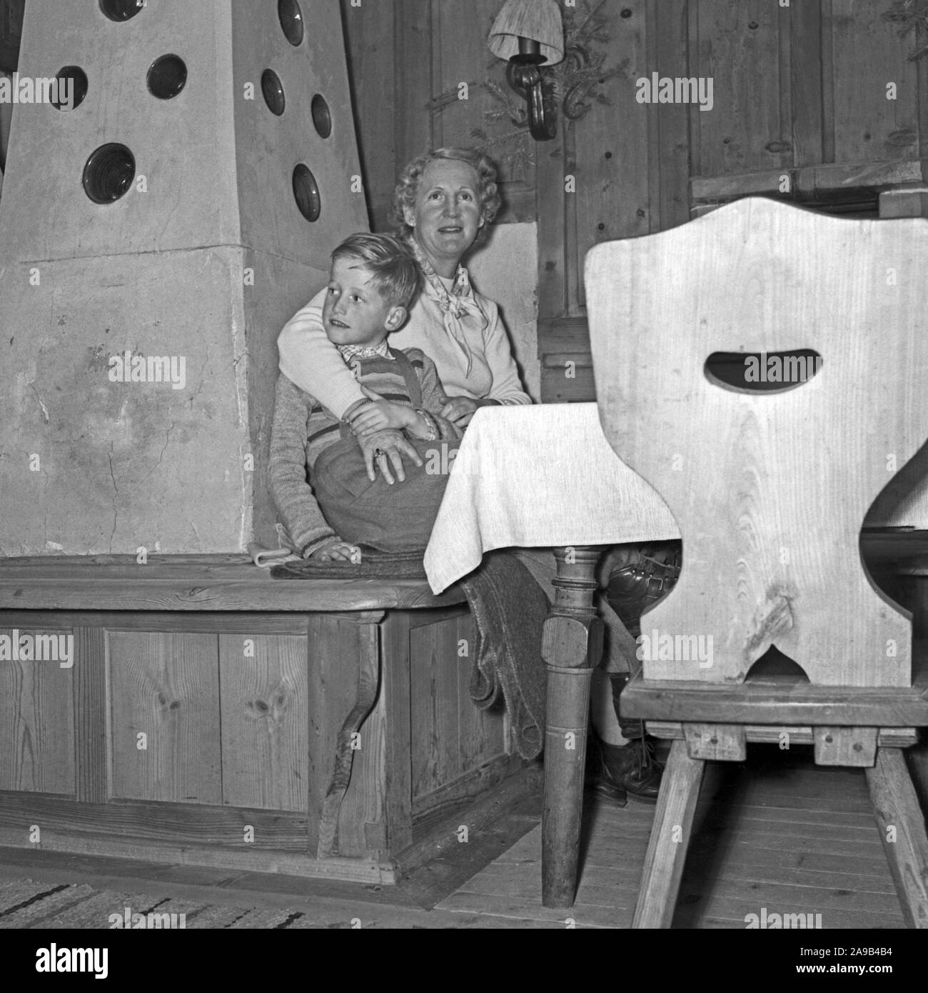 Madre e hijo sentado por la estufa en espera de la Navidad, Alemania 1955 Foto de stock