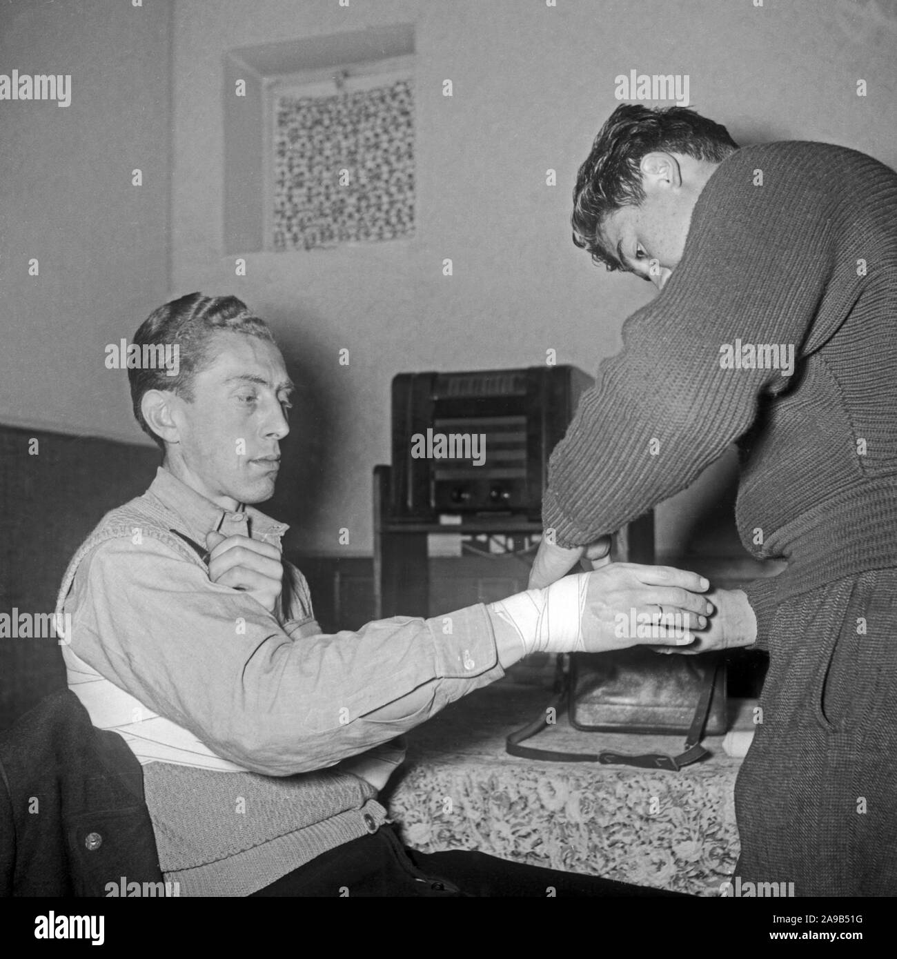 Los hombres aprenden a configurar un vendaje en una lección de primeros auxilios, Alemania 1953 Foto de stock