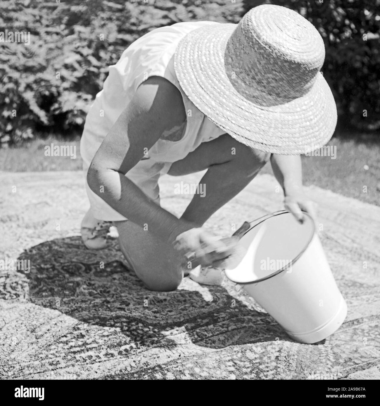 Una mujer trajo una alfombra para el jardín para limpiarlo, Alemania 1958 Foto de stock
