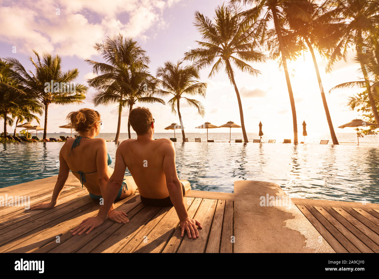 Pareja disfrutando de las vacaciones en la playa en el resort tropical con piscina y palmeras de coco cerca de la costa, con hermosos paisajes al atardecer Foto de stock