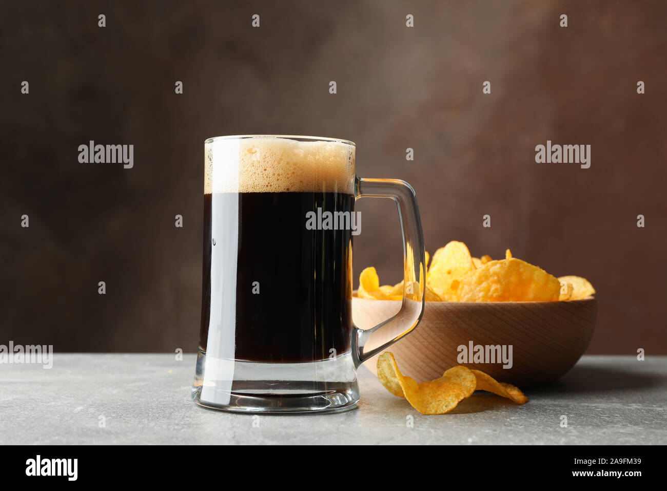 Vaso de cerveza oscura y chips en la tabla gris, espacio para texto Foto de stock