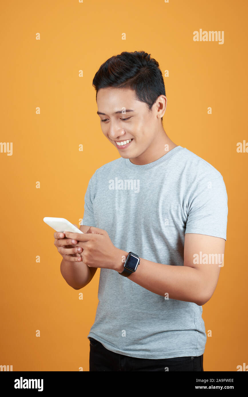 Elegante casual hombre asiático mediante smartphone con fondo naranja. Foto de stock