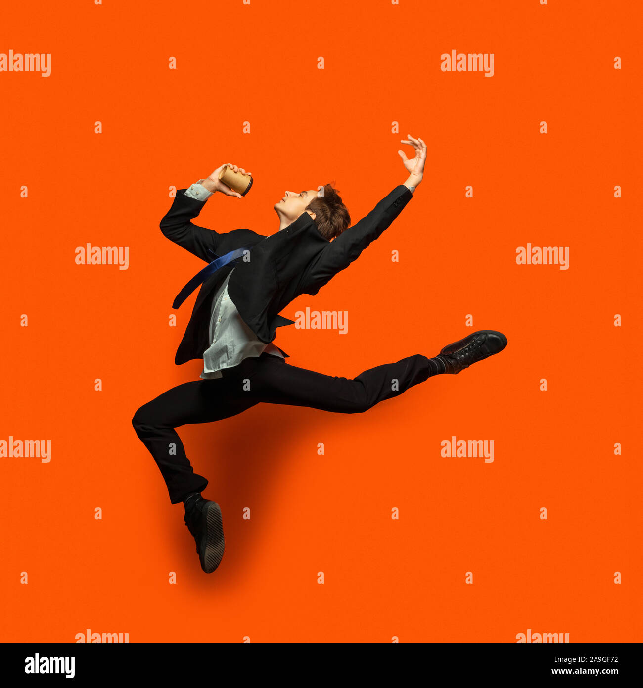 Hombre casual Ropa de estilo Office saltando y bailando aislado sobre fondo de color naranja brillante. Negocios, start-up, el espacio abierto, el concepto de inspiración. El ballet de danza flexible. Apurando, beber café. Foto de stock