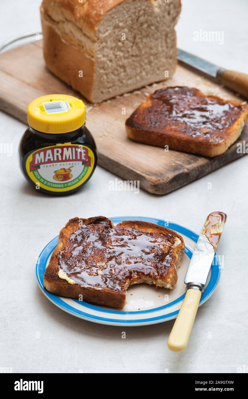 Marmite sobre pan tostado en un plato junto a una hogaza de pan blanco y un frasco de marmite Foto de stock