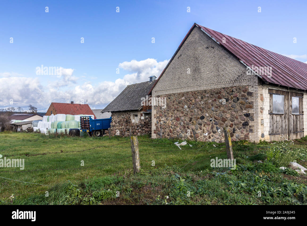 Los graneros de piedra antigua, maquinaria agrícola, un silo de pirámide de paca, verde pradera. Granja de productos lácteos industriales. Podlasie, Polonia. Foto de stock