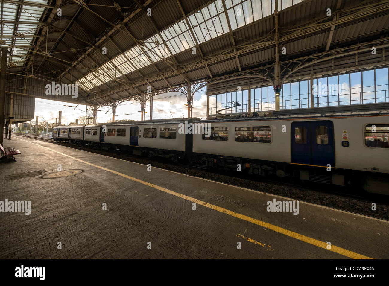 Tren de pasajeros estacionado en una plataforma de estación con una estructura de techo vintage en un día soleado Foto de stock