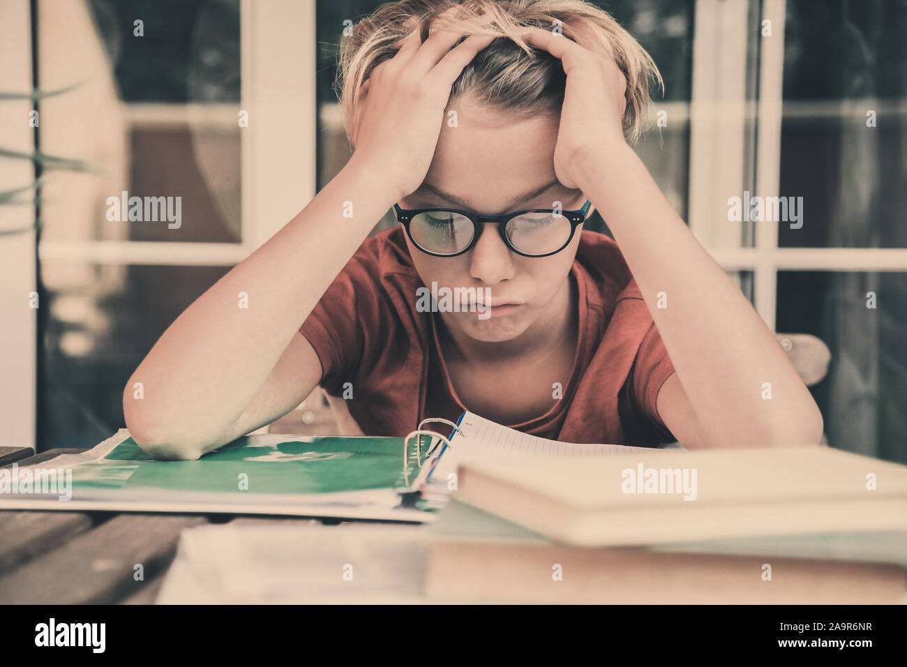 Cansado estudiante haciendo los deberes en casa sentados exterior con libros y periódicos. Chico cansado debido a su gran estudio. Niño dormido en el copybook después l Foto de stock