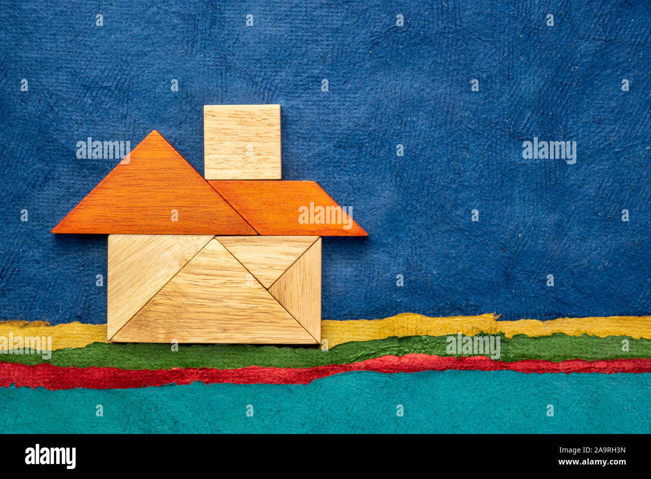 Imagen abstracta de una casa construida a partir de siete piezas de madera tangram contra paisaje creado con coloridas hojas de papel de corteza, copyright por el phot Fotografía de stock -