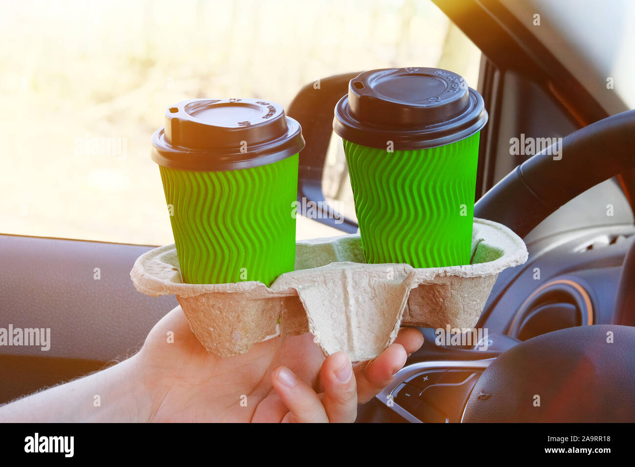 Dos vasos de papel verde con té o café en un lado masculino en coche en  sunny fondo difuminado. Comida para llevar, los medios de comunicación  social. El desayuno por la mañana
