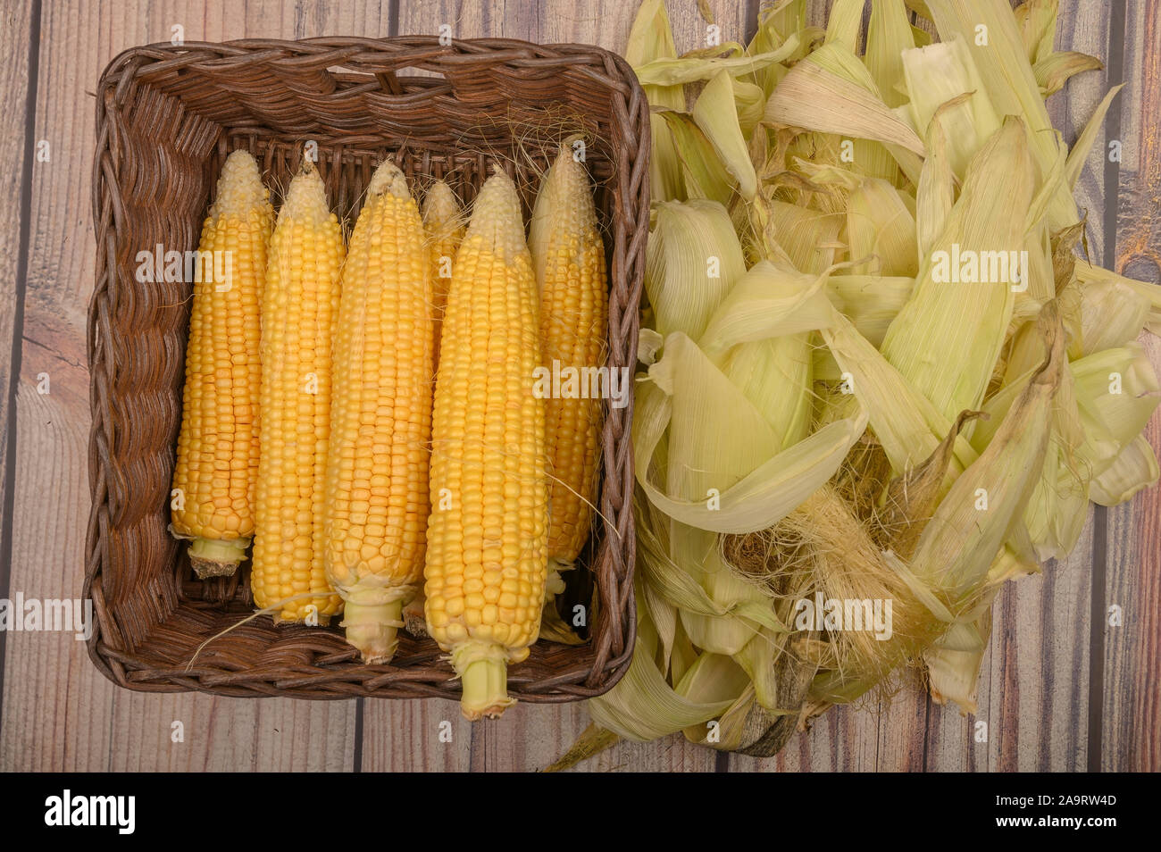 Pelar las mazorcas de maíz en una cesta de mimbre y hojas de maíz sobre una  mesa de madera. Cosecha de Otoño. Dieta de fitness. Dieta saludable. Para  una delicia dulce Fotografía