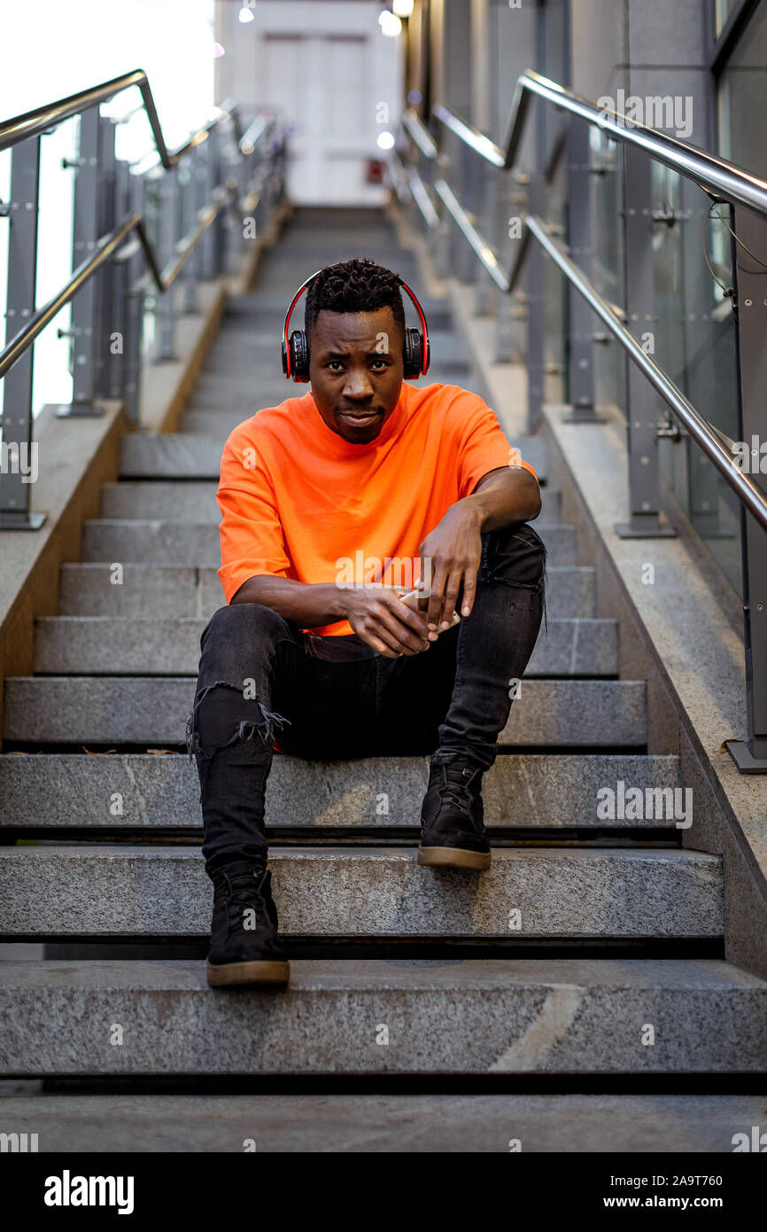 Los jóvenes afroamericanos hombre en elegante color naranja Hoodie  sweatshirt en auriculares inalámbricos, escuchando música y sentado en las  escaleras Fotografía de stock - Alamy