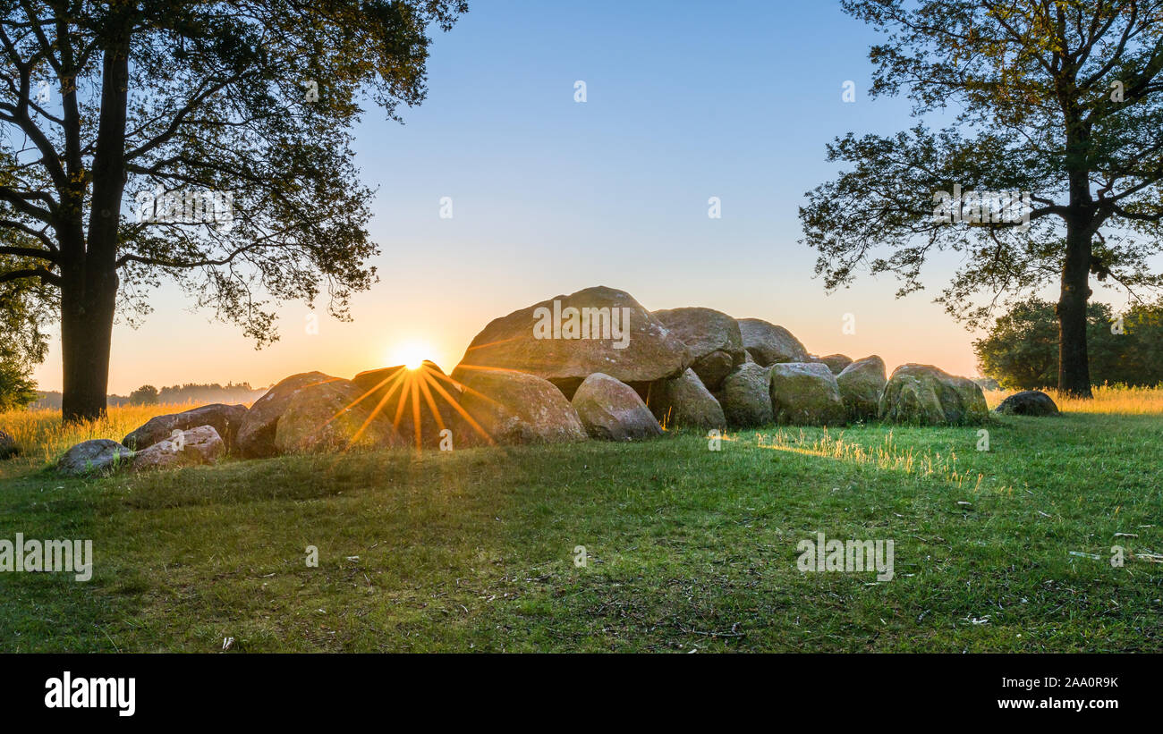 Megalith típico holandés piedras en Drenthe sunrise justo detrás de las piedras con el pasto verde y árboles en el paisaje Foto de stock