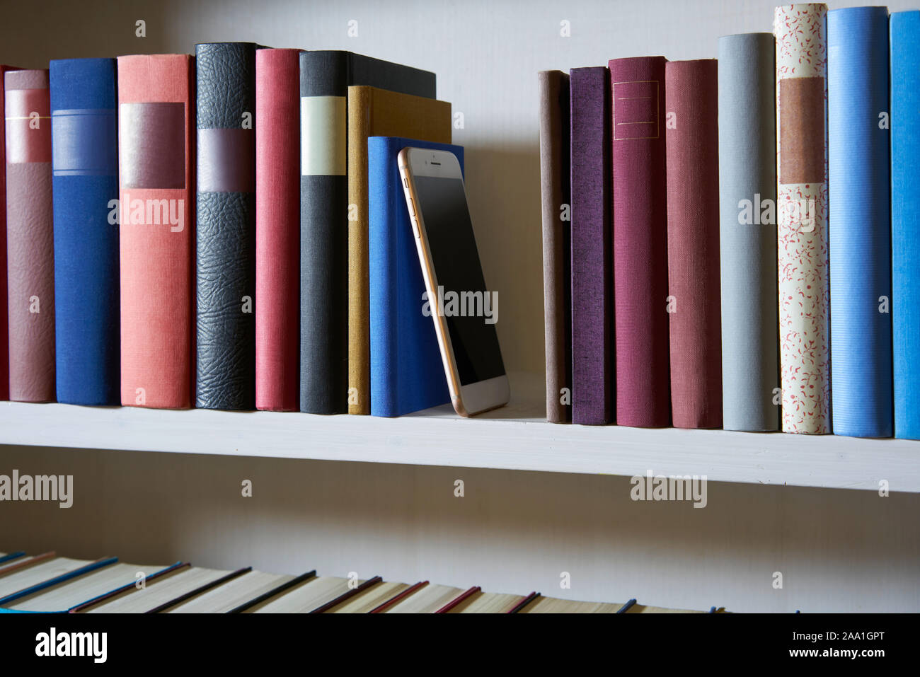 Sideview de un teléfono móvil en una estantería de libros entre los libros Foto de stock