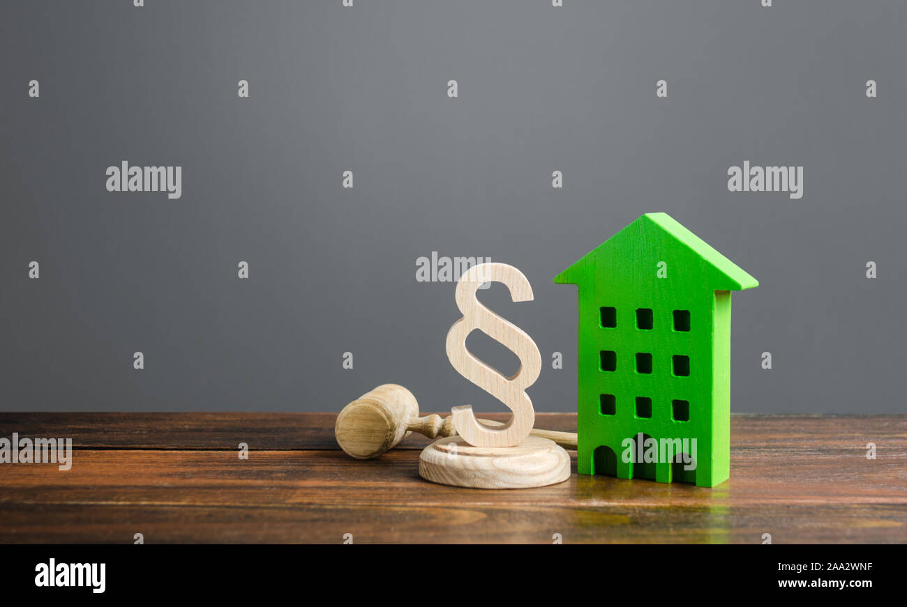La casa verde y el párrafo figurine con un martillo de juez. Los litigios en disputas de bienes raíces y vivienda. Normas y reglas para la construcción y mantenimiento. Foto de stock