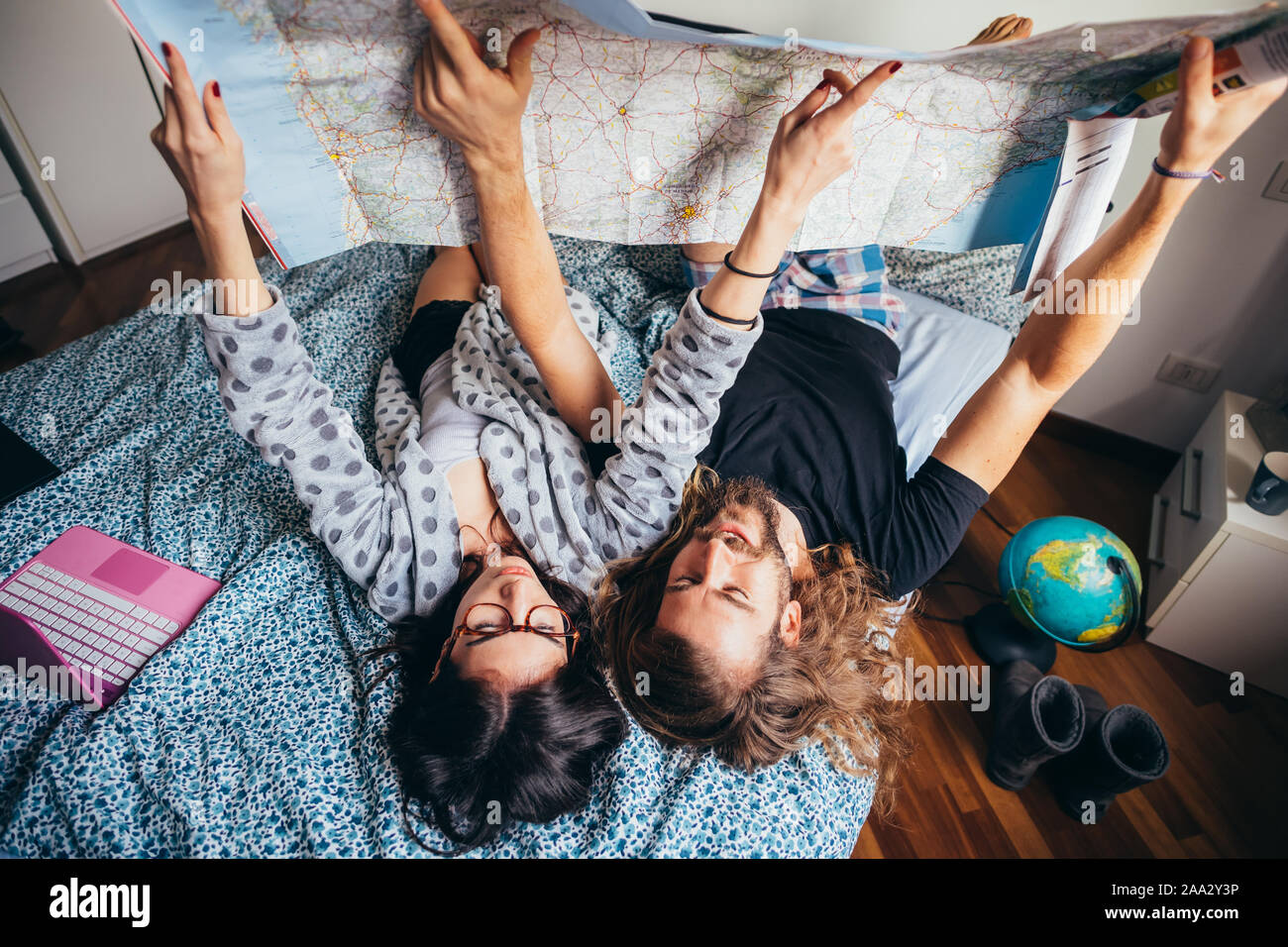 Pareja joven tumbado en la cama planeando viajar leer mapa - viajero, vacaciones, concepto de planificación Foto de stock