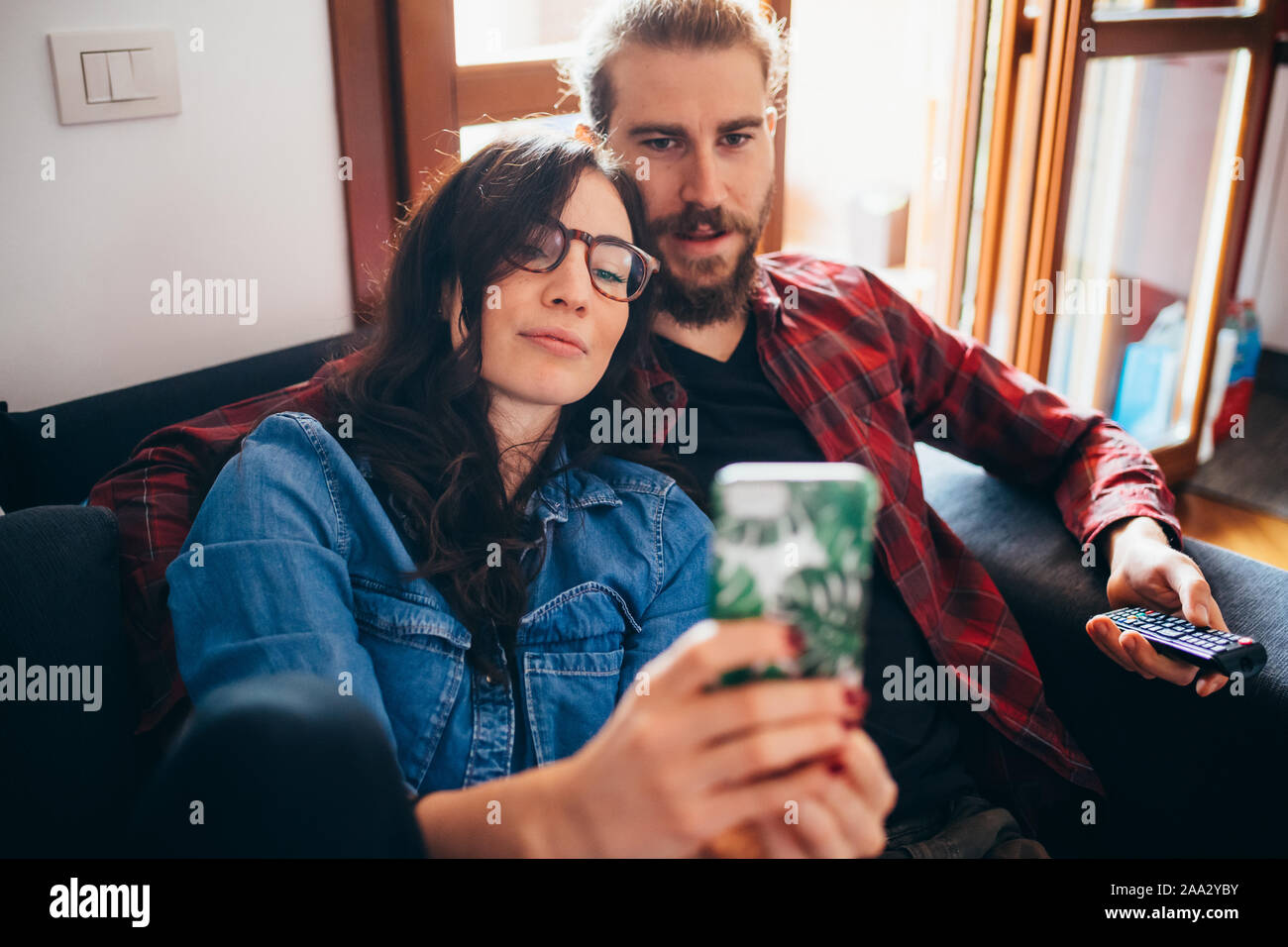 Hermosa joven feliz pareja sofá interiores domésticos teniendo selfie utilizando smartphones - tecnología, screentime, freetime concepto Foto de stock