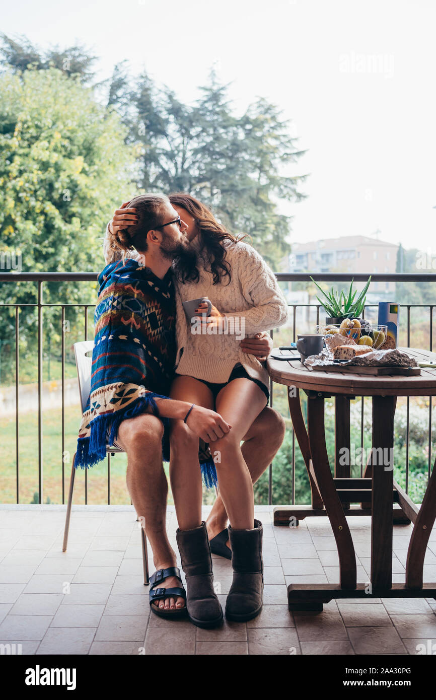 Pareja joven en casa terraza desayunando besos - ella está sentado en su regazo, amor, relación, romance concepto Foto de stock
