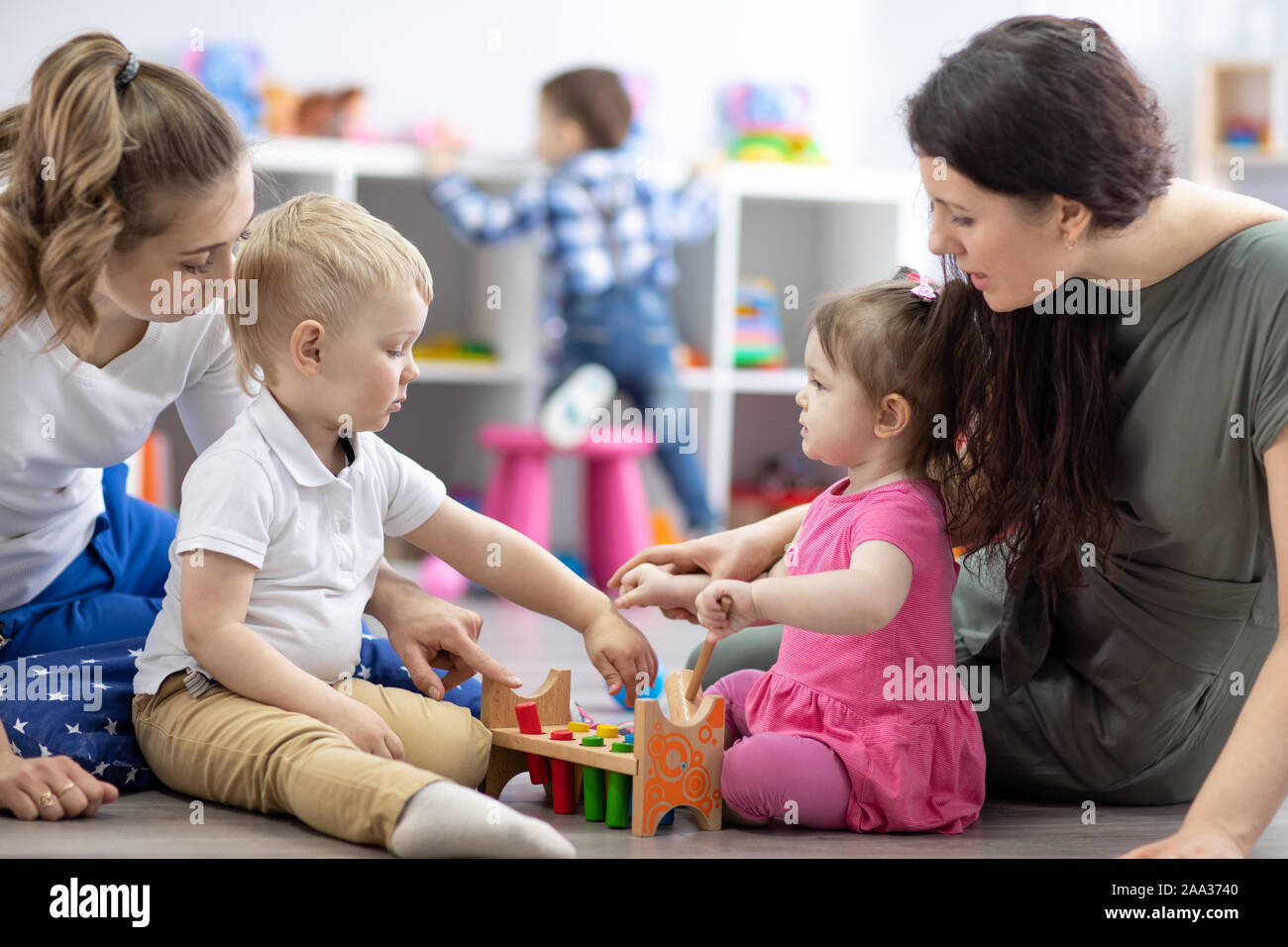 Poco bebés kid niño chico y chica con las mamás juegan juntos en la sala de párvulos. Niños en edad preescolar en guarderías Foto de stock