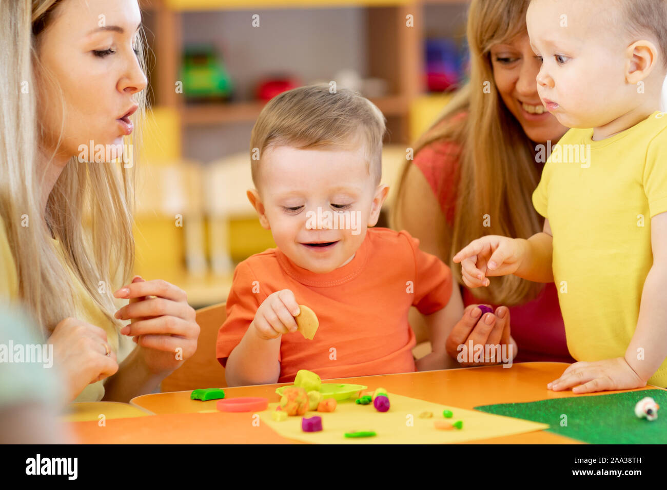 Niños pequeños se divierten juntos con las mamás. Creative Kids moldura en casa. Los niños chicos jugando con plastilina o masa. Foto de stock