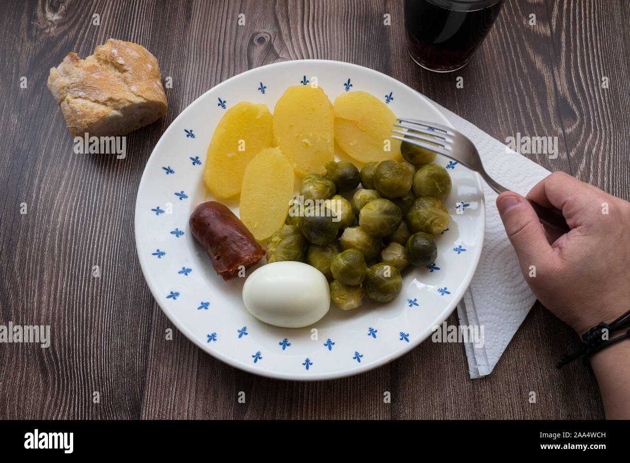 Placa con las coles de Bruselas, salchichas, patatas cocidas y huevo junto a la mano que sujeta la horquilla Foto de stock