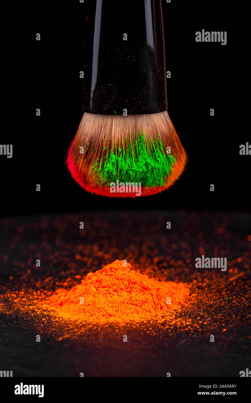 Mejilla cepillo con neón colorido polvo cosmético montón sobre fondo negro Foto de stock