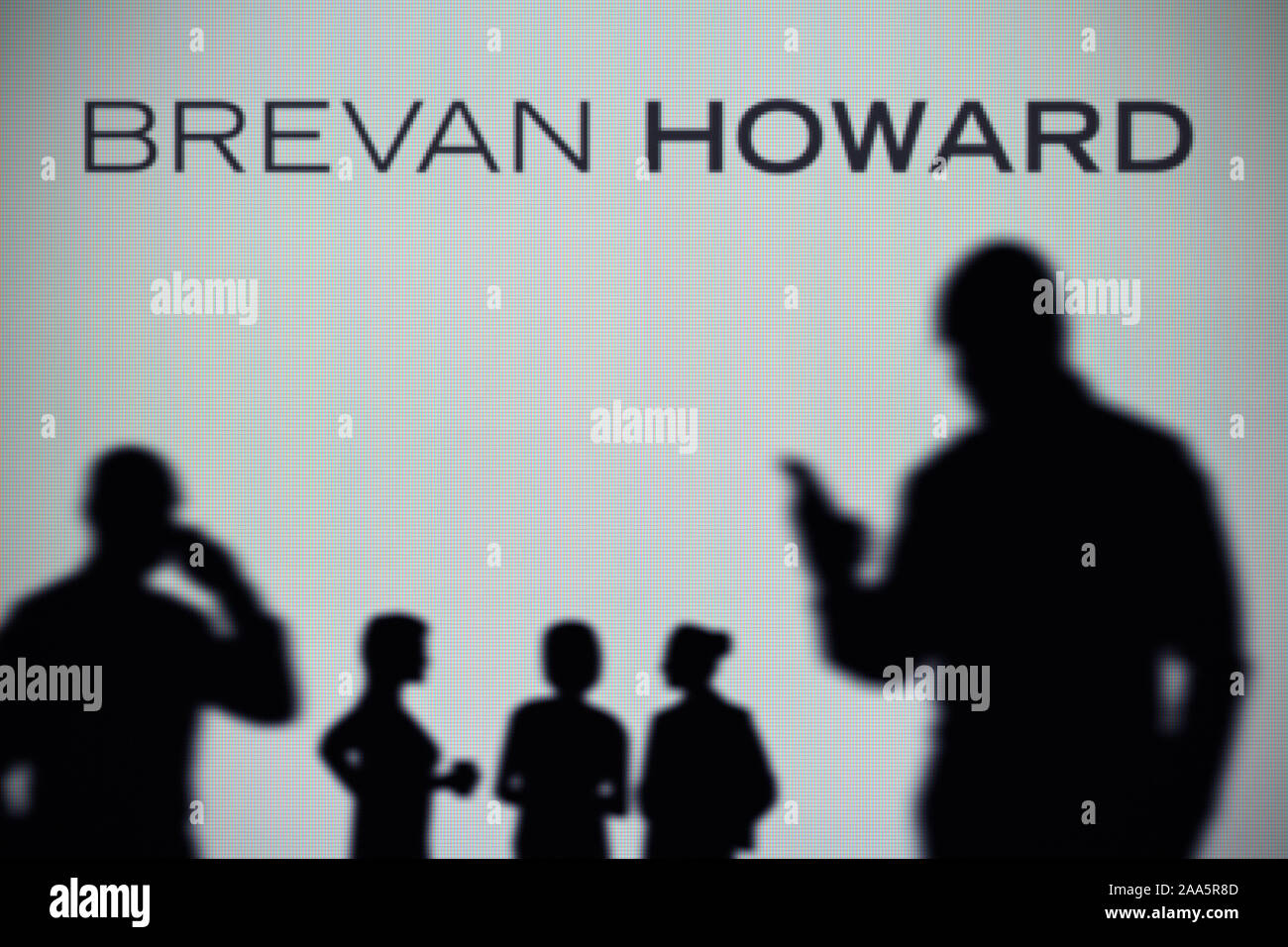 El Brevan Howard logo es visto en una pantalla LED en el fondo mientras una silueta persona utiliza un smartphone (uso Editorial solamente) Foto de stock