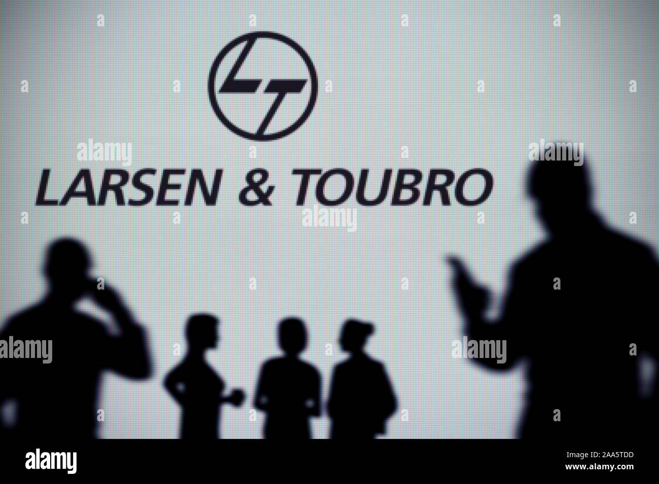 El Larsen and Toubro logo es visto en una pantalla LED en el fondo mientras una silueta persona utiliza un smartphone (uso Editorial solamente) Foto de stock