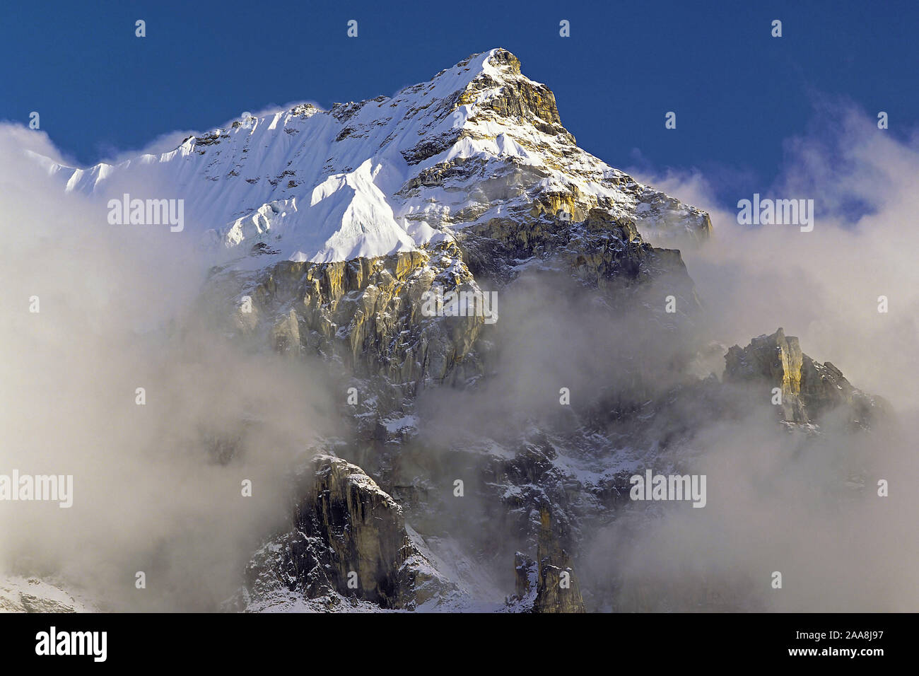 Por la tarde la niebla y las nubes se reúnen alrededor de los espectaculares riscos y la cumbre de un pico sin nombre en la región oriental del Nepal Kangchenjunga Foto de stock