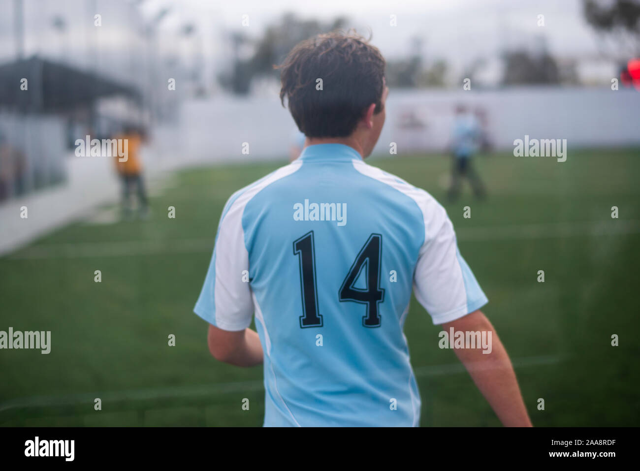Adolescente jugando fútbol vistiendo una luz azul jersey número 14. Foto de stock