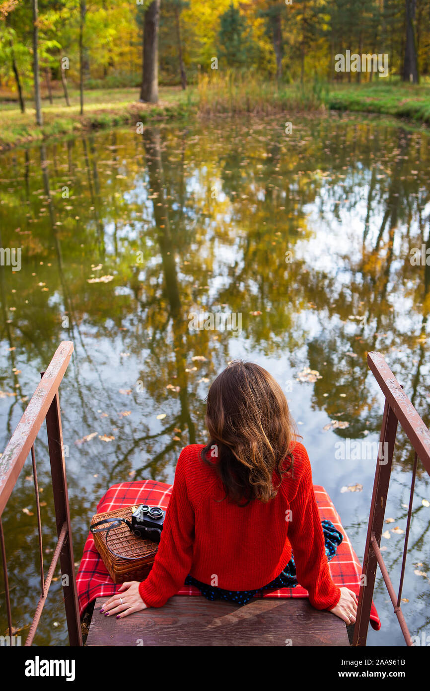 Una joven mujer sentada con su espalda en un puente cerca de un lago en un  día soleado. Bello otoño Fotografía de stock - Alamy