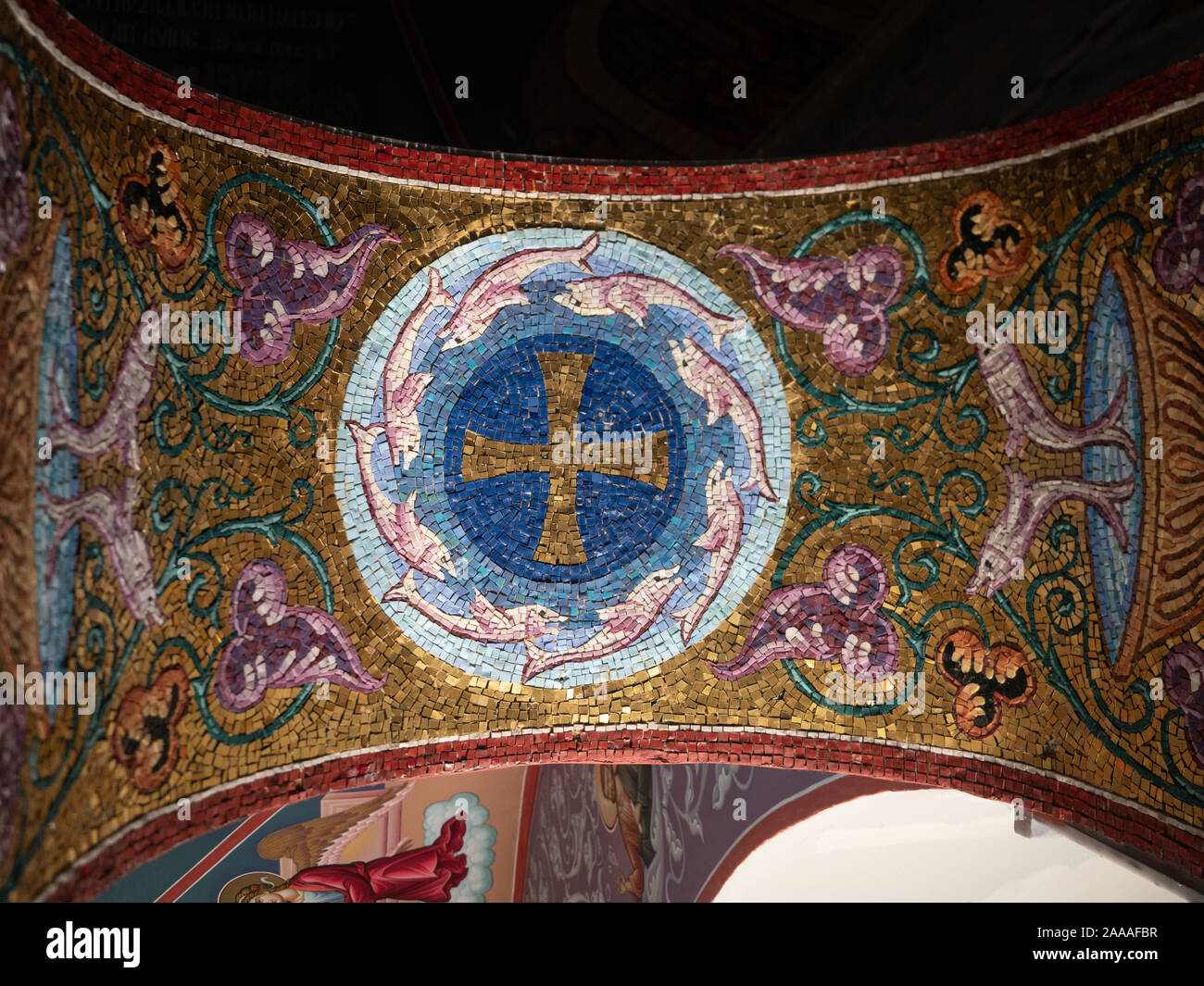 Cerca de intrincado mosaico con fondo de oro, una cruz, delfines o marsopas, flores y vides que decoran un arco en la Bapistery de St. Foto de stock