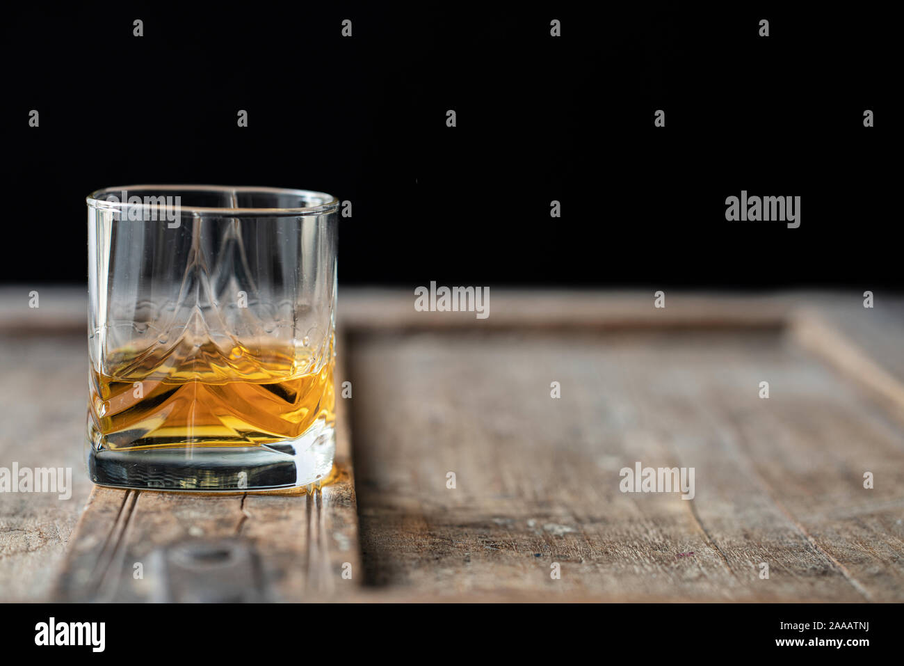 Primer plano de un vaso de whisky en una vieja mesa de madera mal utilizado, fondo oscuro Foto de stock