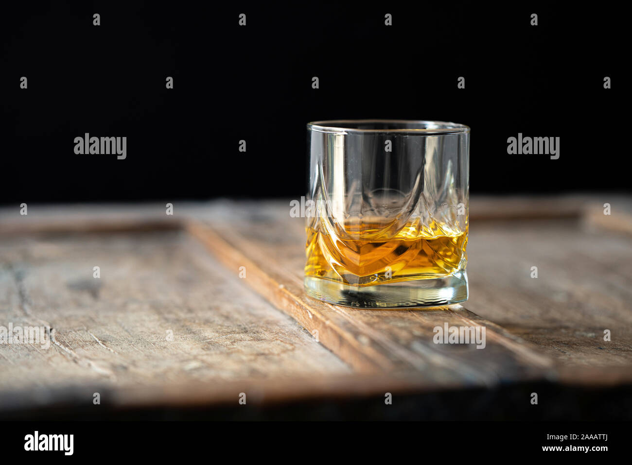 Primer plano de un vaso de whisky en una vieja mesa de madera mal utilizado, fondo oscuro Foto de stock