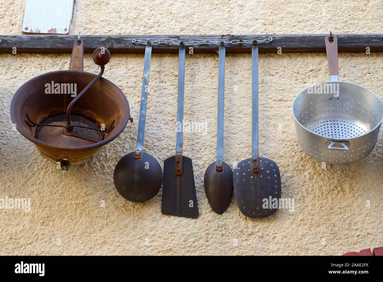 Vintage o antigua colección de antiguos utensilios de cocina colgados en las estanterías de pared incluyendo sartenes, espátulas y Drainers Foto de stock